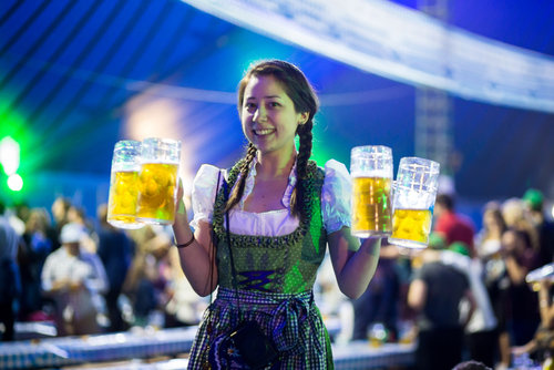 An attractive young woman holding four steins of beer at the Oktoberfest celebration.